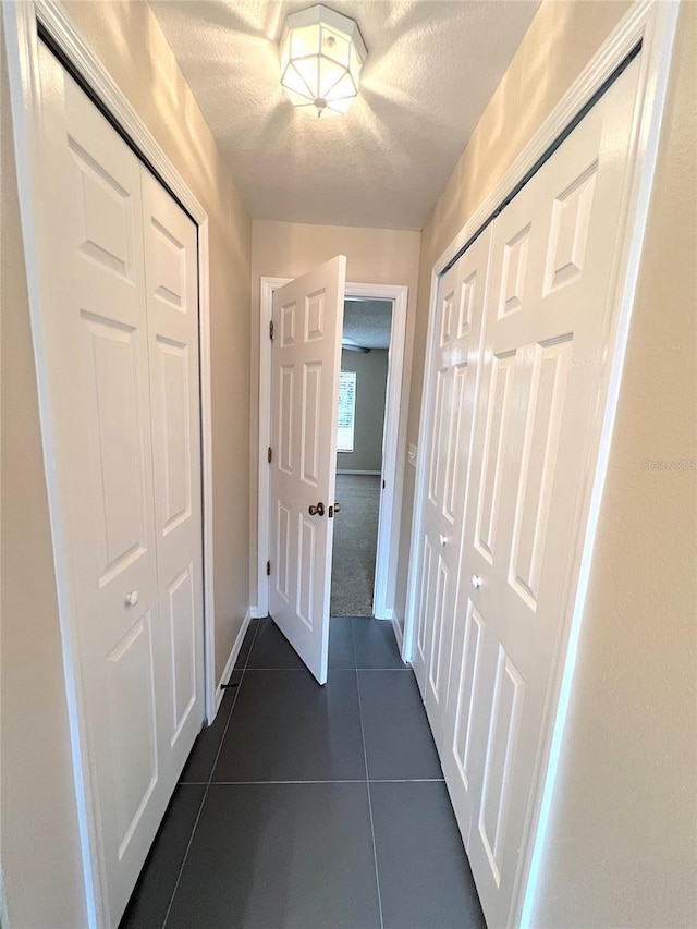 hallway featuring a textured ceiling and dark tile patterned floors