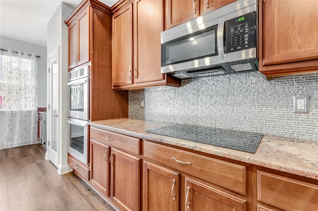 kitchen with stainless steel appliances, decorative backsplash, light stone counters, and light hardwood / wood-style flooring