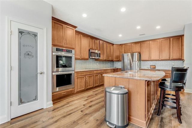 kitchen featuring light hardwood / wood-style floors, appliances with stainless steel finishes, light stone countertops, and an island with sink