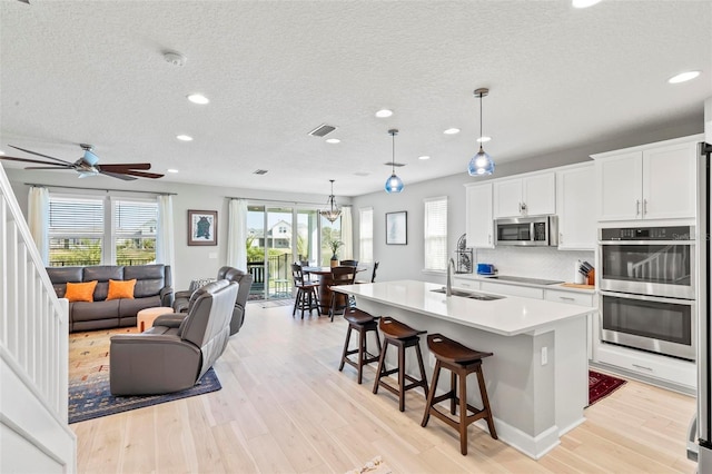 kitchen featuring sink, stainless steel appliances, decorative light fixtures, and an island with sink