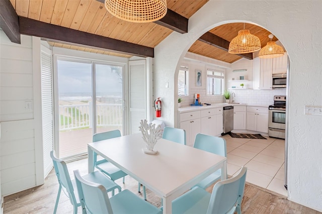 dining space with arched walkways, light wood finished floors, a textured wall, lofted ceiling with beams, and wood ceiling