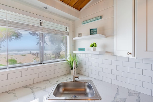 kitchen featuring open shelves, lofted ceiling, white cabinets, a sink, and light stone countertops