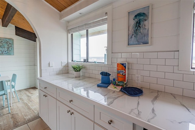 kitchen featuring beam ceiling, white cabinetry, and light stone countertops