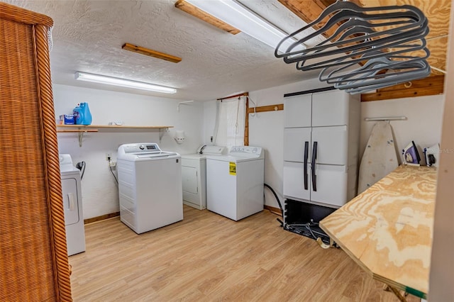 clothes washing area with light wood-type flooring, washing machine and dryer, laundry area, and a textured ceiling