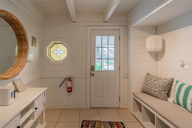 interior space featuring light tile patterned floors, wood walls, wainscoting, and beam ceiling