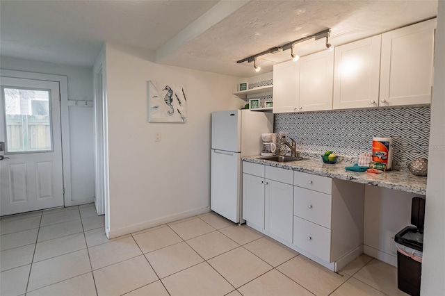 kitchen with tasteful backsplash, light tile patterned flooring, a sink, and freestanding refrigerator