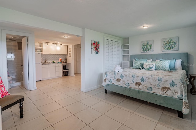 bedroom featuring light tile patterned floors, ensuite bath, baseboards, and freestanding refrigerator