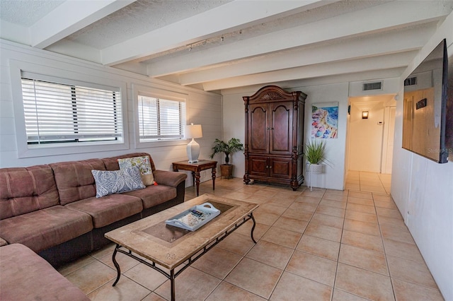 living area with a textured ceiling, beamed ceiling, light tile patterned flooring, and visible vents