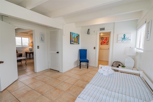 bedroom featuring light tile patterned floors, beamed ceiling, visible vents, and baseboards