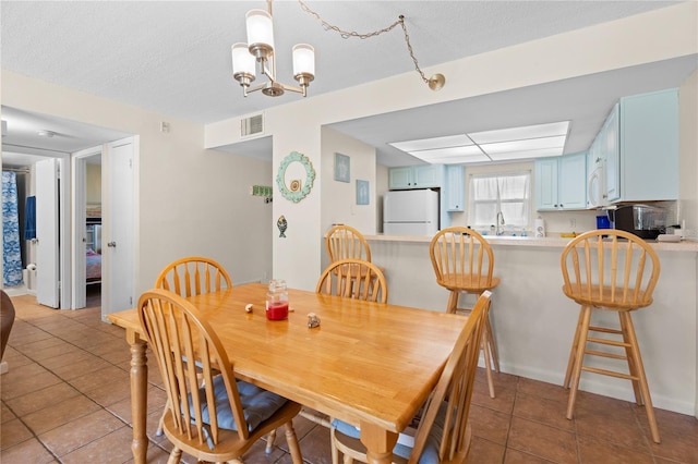 dining room featuring light tile patterned flooring, an inviting chandelier, sink, and a textured ceiling