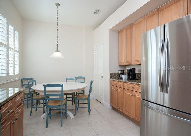 kitchen featuring hanging light fixtures, light stone counters, stainless steel refrigerator, and light tile patterned floors