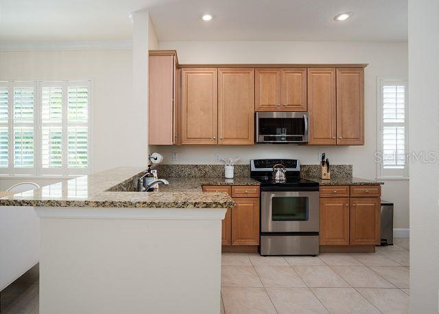 kitchen featuring light stone counters, crown molding, light tile patterned floors, appliances with stainless steel finishes, and kitchen peninsula