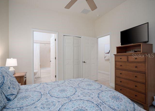 tiled bedroom with ceiling fan, connected bathroom, and a closet