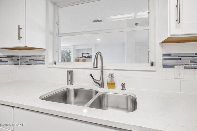 room details featuring tasteful backsplash, white cabinetry, light stone countertops, and sink