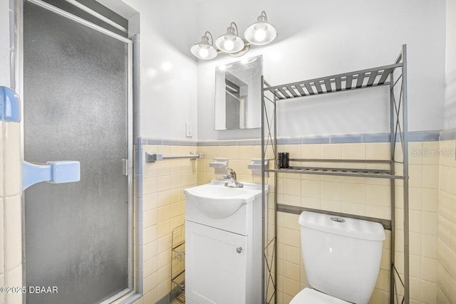 bathroom with vanity, a shower with shower door, tile walls, and toilet