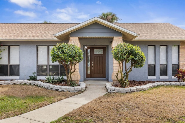 entrance to property featuring roof with shingles, a lawn, and stucco siding