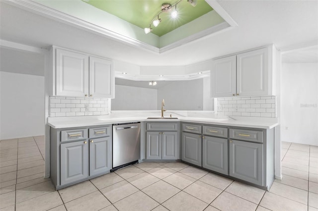 kitchen featuring gray cabinetry, a sink, a tray ceiling, light countertops, and dishwasher