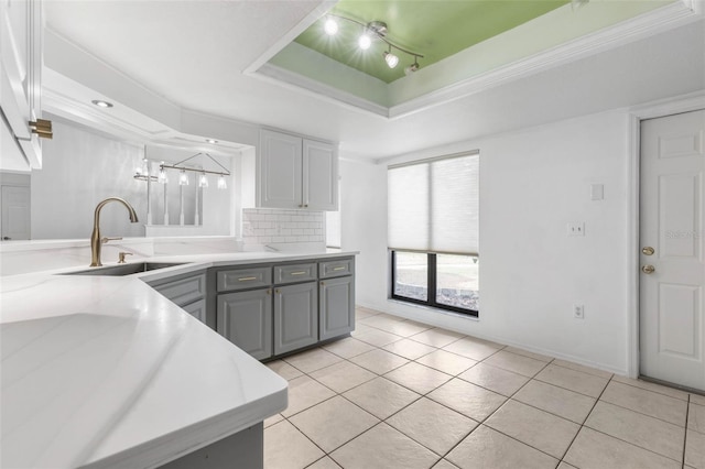 kitchen with backsplash, gray cabinetry, a tray ceiling, light tile patterned floors, and a sink
