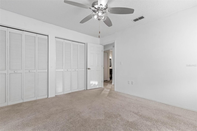 unfurnished bedroom with visible vents, multiple closets, a textured ceiling, carpet floors, and ceiling fan