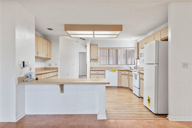 kitchen with white appliances, kitchen peninsula, a textured ceiling, and light parquet floors