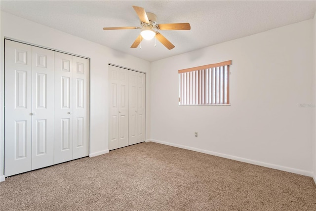 unfurnished bedroom with ceiling fan, carpet floors, a textured ceiling, and two closets