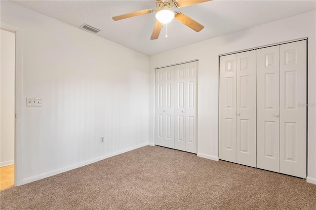 unfurnished bedroom featuring multiple closets, ceiling fan, and carpet flooring