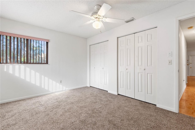 unfurnished bedroom with ceiling fan, a textured ceiling, multiple closets, and carpet flooring