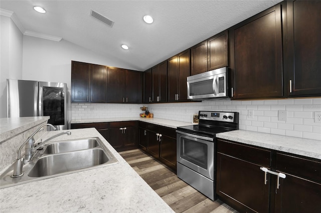 kitchen featuring vaulted ceiling, appliances with stainless steel finishes, sink, decorative backsplash, and light wood-type flooring