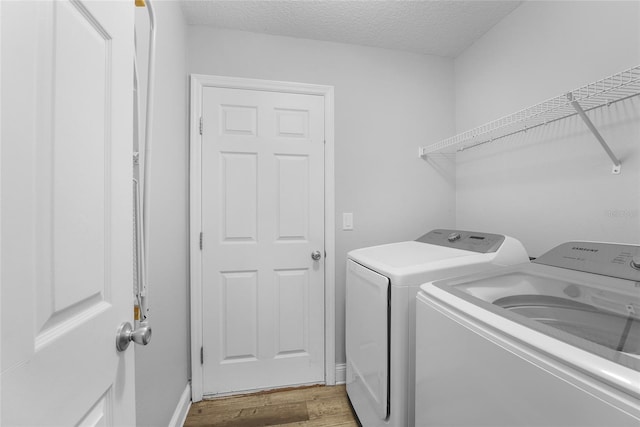 clothes washing area with washing machine and clothes dryer, a textured ceiling, and light hardwood / wood-style flooring