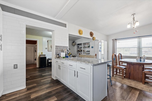 kitchen featuring light stone countertops, a breakfast bar area, white cabinetry, and dark wood-style flooring