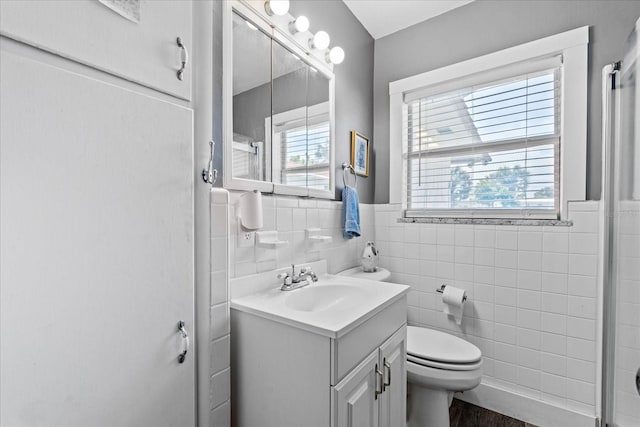 full bath with toilet, plenty of natural light, tile walls, and vanity