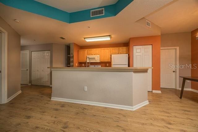 kitchen featuring light brown cabinetry, white appliances, a center island, and light wood-type flooring