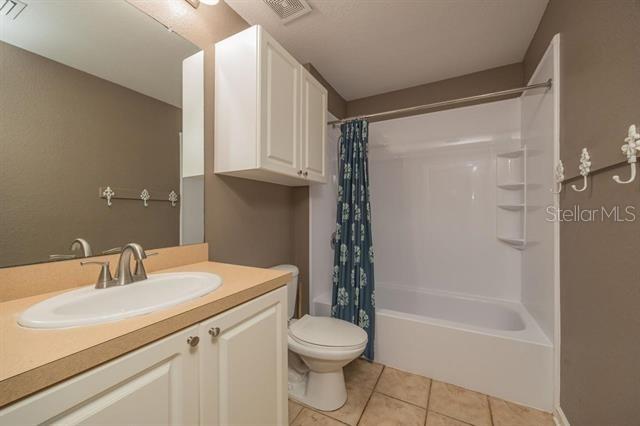 full bathroom with shower / bathtub combination with curtain, tile patterned floors, toilet, and vanity