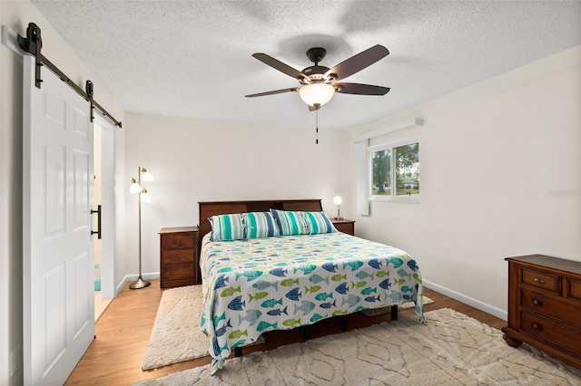 bedroom featuring ceiling fan, a barn door, a textured ceiling, and light hardwood / wood-style flooring