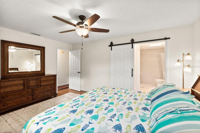 bedroom with connected bathroom, ceiling fan, a barn door, and a textured ceiling