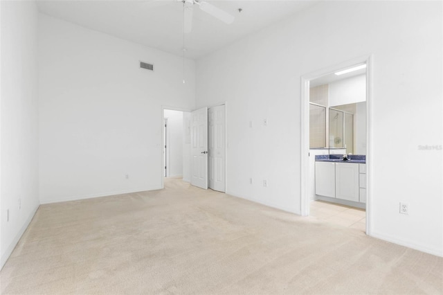 unfurnished bedroom featuring a high ceiling, connected bathroom, and light carpet