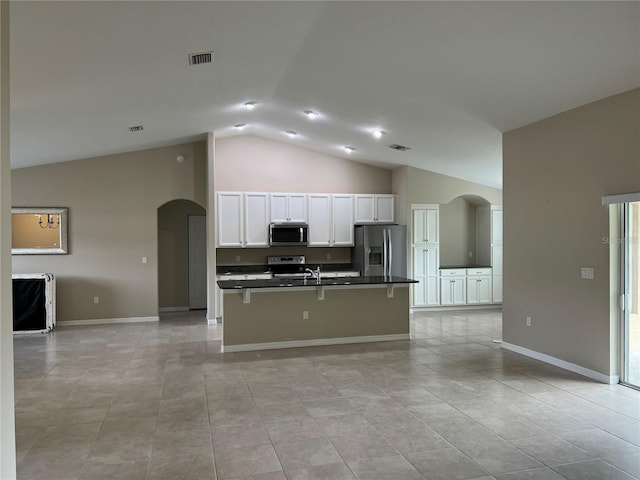 kitchen featuring vaulted ceiling, appliances with stainless steel finishes, white cabinetry, a breakfast bar area, and a center island with sink