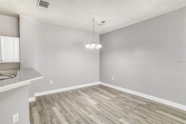 unfurnished dining area featuring sink, a chandelier, and light wood-type flooring