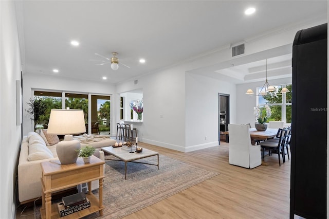 living room featuring crown molding, a tray ceiling, ceiling fan with notable chandelier, and light hardwood / wood-style flooring