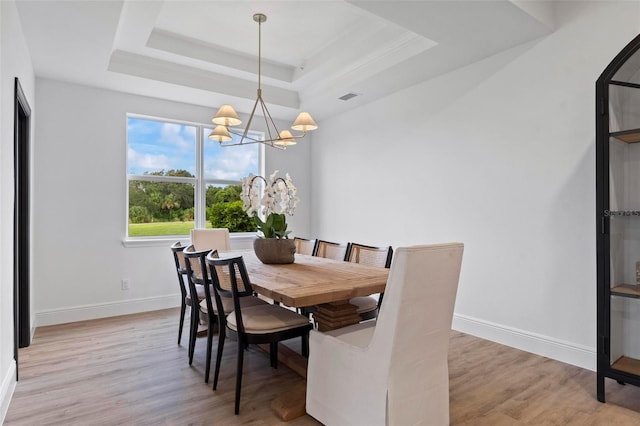 dining space with a raised ceiling, an inviting chandelier, and light wood-type flooring