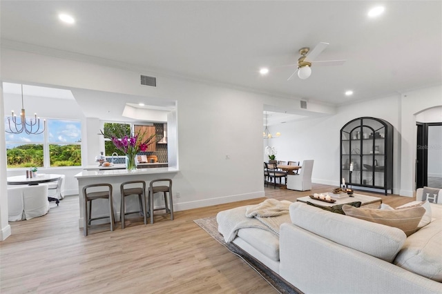 living room featuring ceiling fan with notable chandelier, ornamental molding, and light wood-type flooring