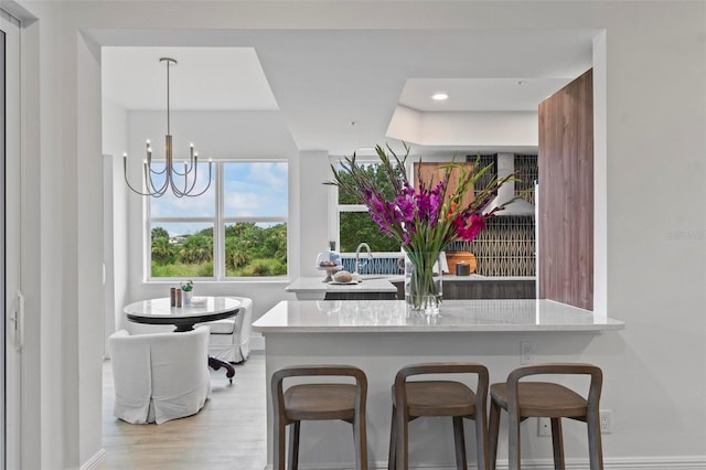 kitchen featuring a breakfast bar, an inviting chandelier, decorative light fixtures, kitchen peninsula, and light hardwood / wood-style floors