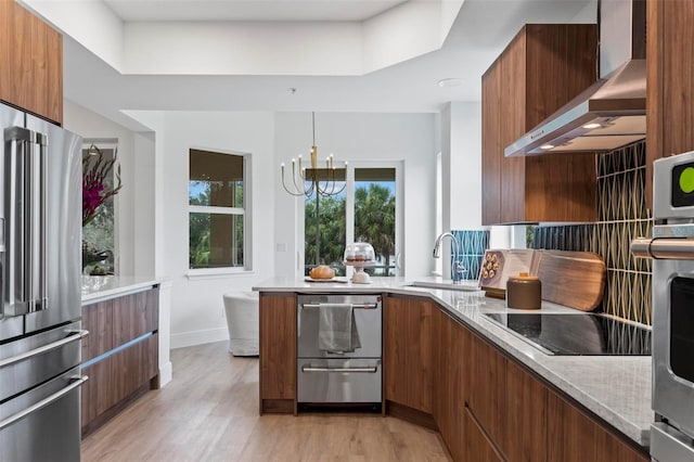 kitchen featuring sink, light stone counters, black electric cooktop, high end refrigerator, and wall chimney exhaust hood