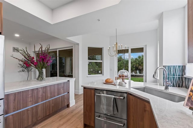 kitchen featuring sink, a chandelier, light hardwood / wood-style flooring, stainless steel dishwasher, and light stone countertops