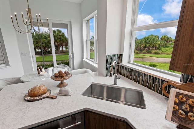 kitchen with sink, pendant lighting, light stone counters, and an inviting chandelier