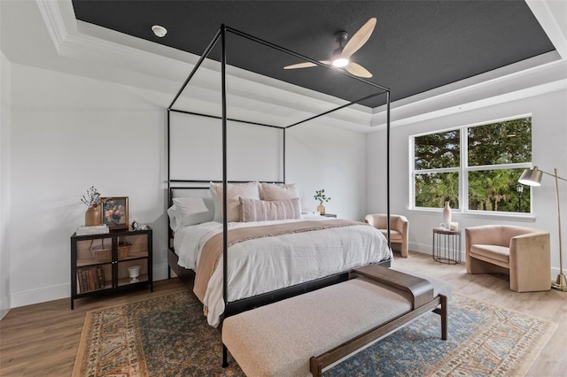 bedroom featuring ceiling fan, wood-type flooring, and a tray ceiling