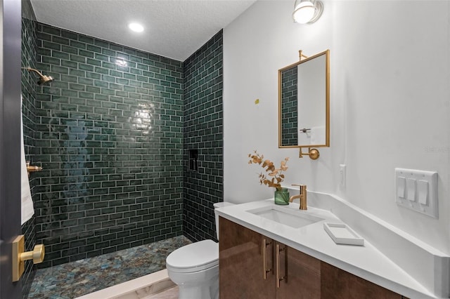 bathroom featuring tiled shower, vanity, toilet, and a textured ceiling