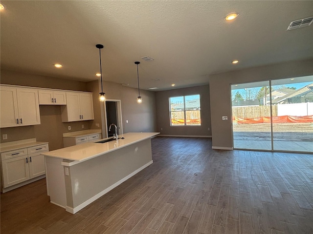 kitchen with hanging light fixtures, white cabinetry, sink, and a kitchen island with sink