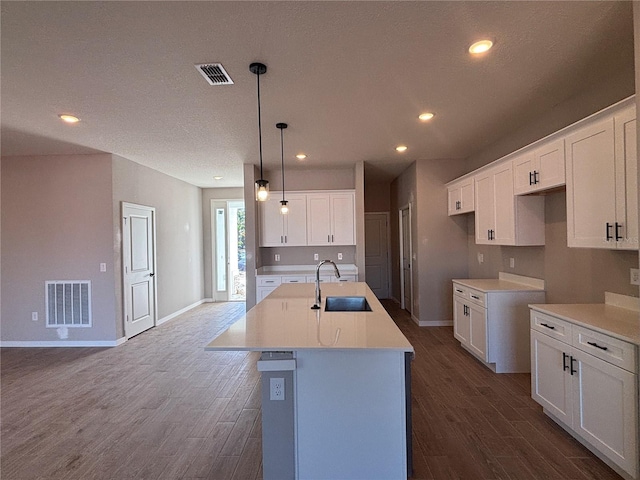 kitchen featuring sink, white cabinets, dark hardwood / wood-style flooring, hanging light fixtures, and a center island with sink