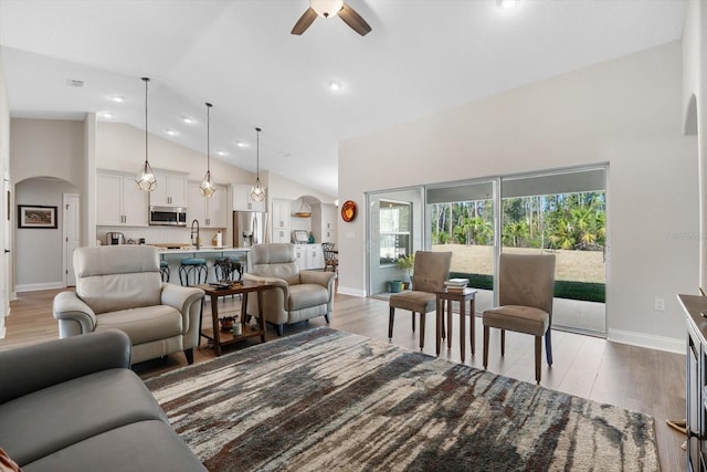 living room with ceiling fan, sink, high vaulted ceiling, and light hardwood / wood-style floors